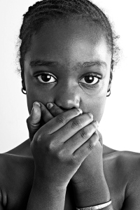 A black-and-white image of a black teenage girl, covering her mouth with her hands.