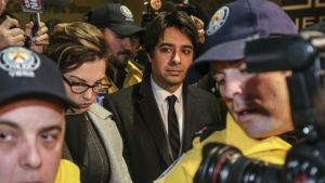 Media image of Jian Ghomeshi, in suit and tie, with journalists and cameramen visible in the foreground.